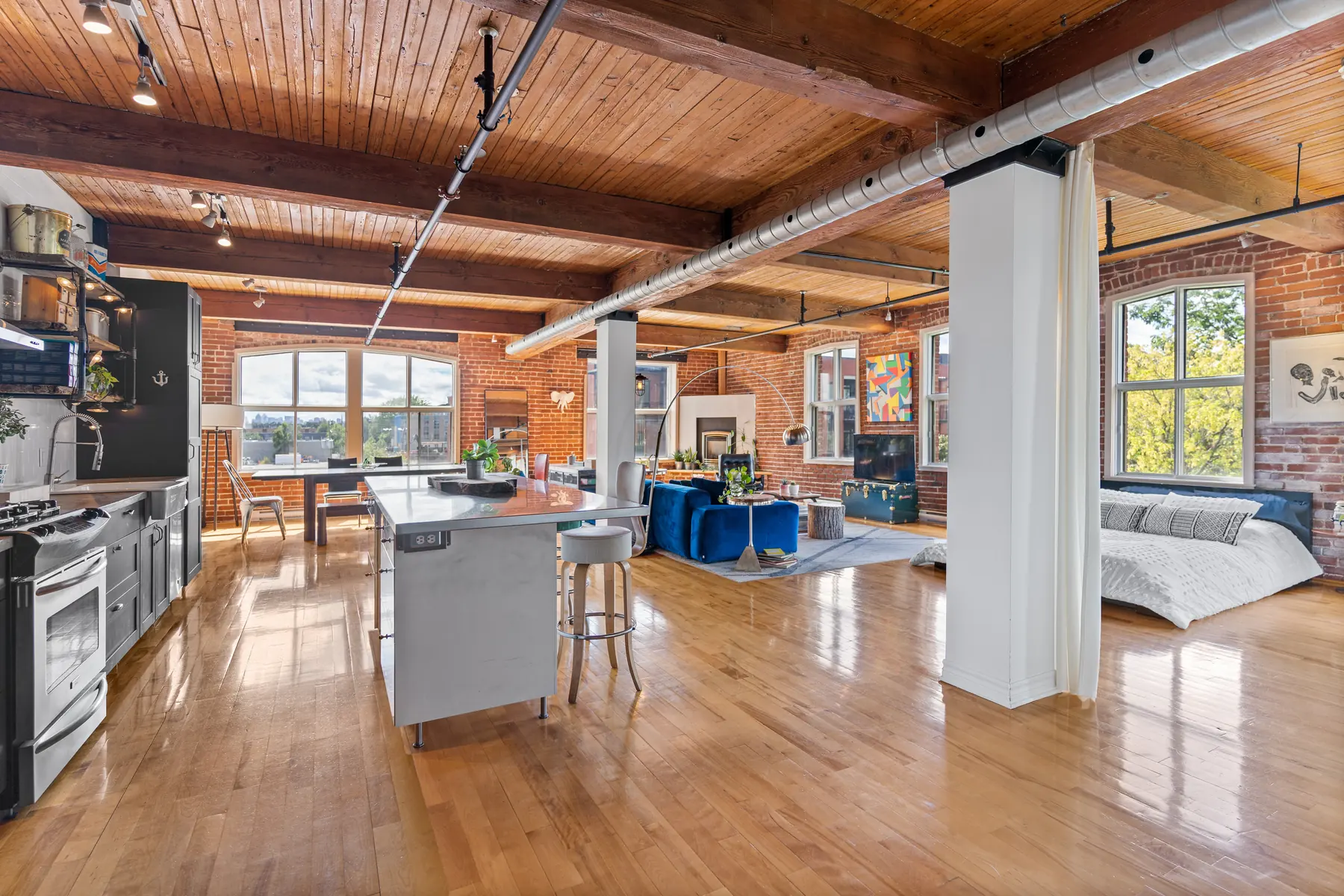 Loft de brique et de bois : poutres, plafond de planches, colonne blanche et plancher d'érable
