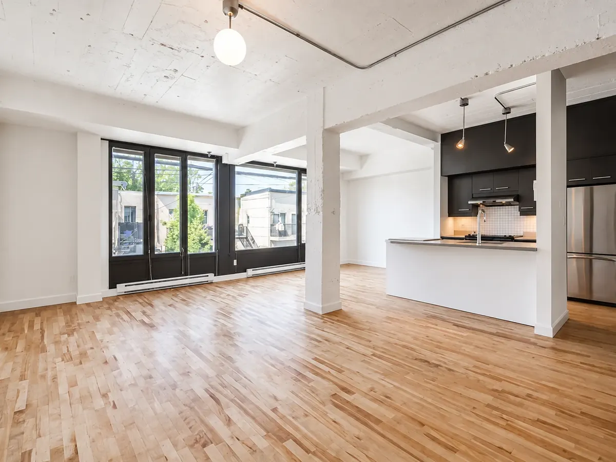 Intérieur d'une unité du 6740, avenue de Gaspé : îlot de cuisine, grandes fenêtres noires et plancher de bois blond