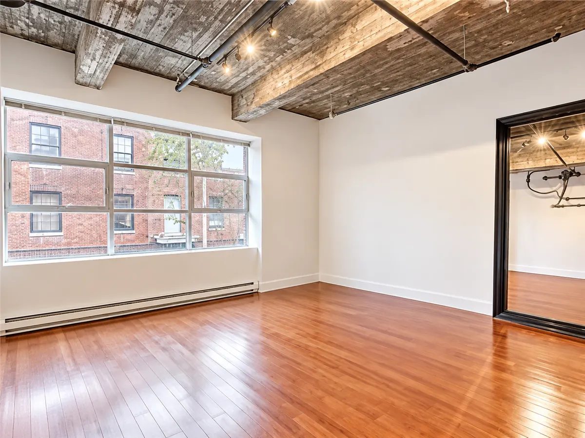 Intérieur d'un loft de Craig's Lofts : fenêtres sur la brique voisine, poutres apparentes et plancher de bois
