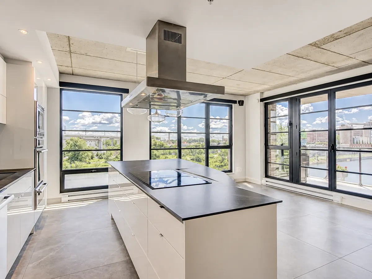 Intérieur d'une unité des Lofts Gallery sur le Canal : cuisine à îlot, hotte au plafond et grandes fenêtres noires