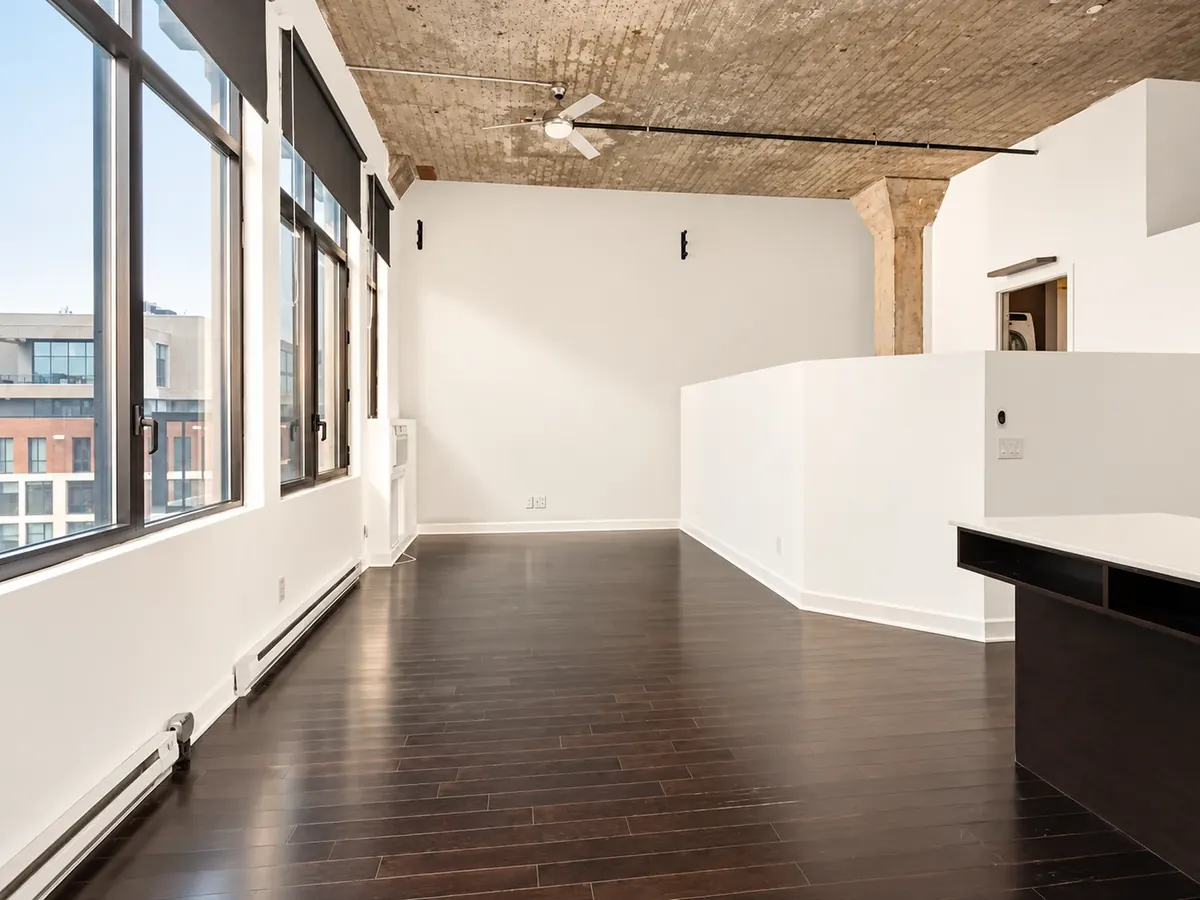 Intérieur d'un loft des Lofts Impérial : plafond de béton, hautes fenêtres et plancher de bois foncé
